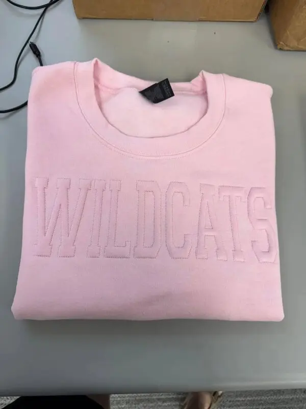 A pink sweatshirt with the word wildcats on it.