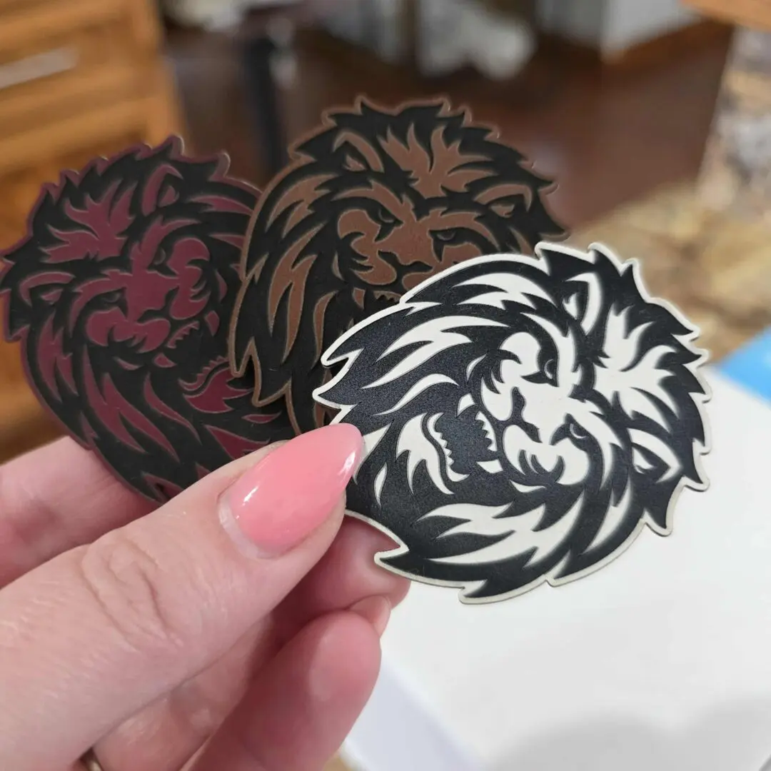 Hand holding three lion face stickers.