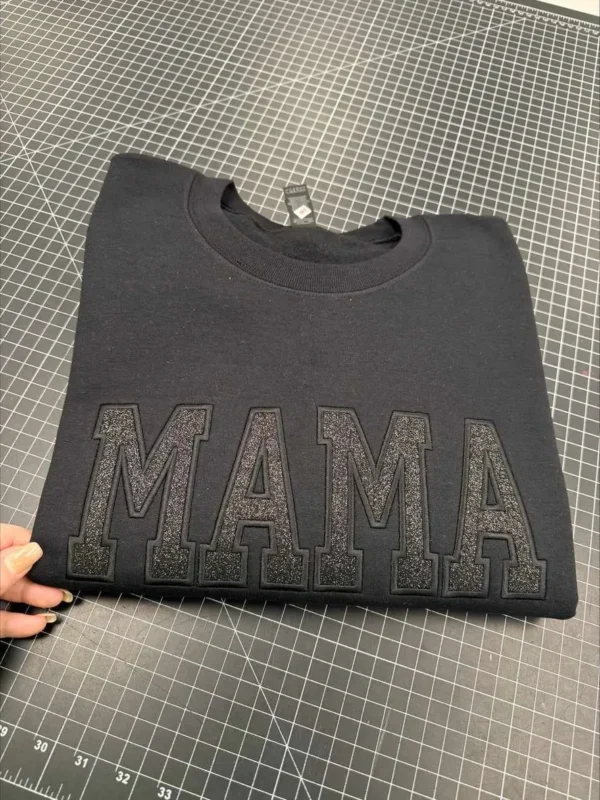Black "MAMA" sweatshirt on grid background.